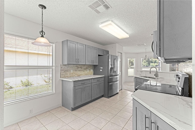 kitchen with gray cabinets, pendant lighting, sink, stainless steel fridge, and stove