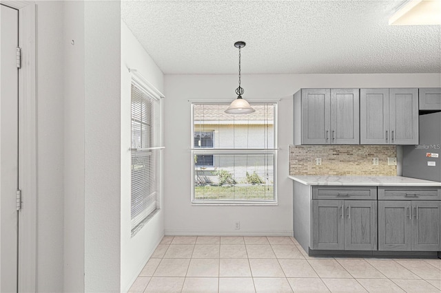 kitchen with pendant lighting, light tile patterned floors, gray cabinetry, backsplash, and fridge