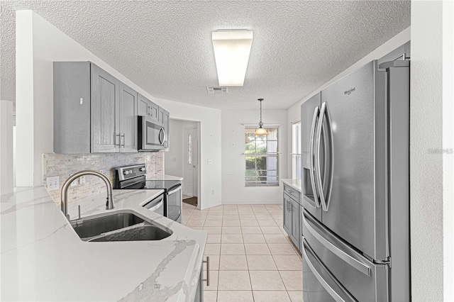 kitchen featuring sink, light tile patterned floors, gray cabinets, appliances with stainless steel finishes, and decorative backsplash