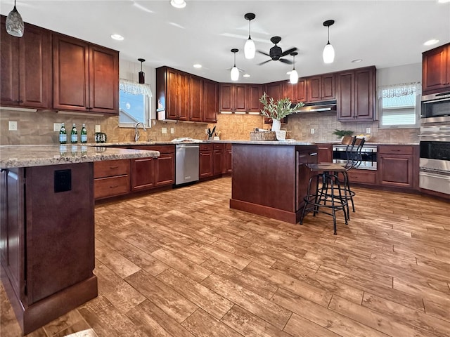 kitchen featuring a breakfast bar area, wood finished floors, a center island, hanging light fixtures, and light stone countertops