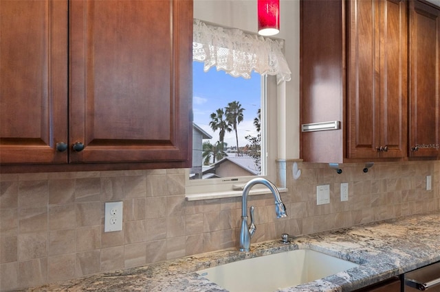 kitchen with light stone counters, brown cabinetry, a sink, and decorative backsplash