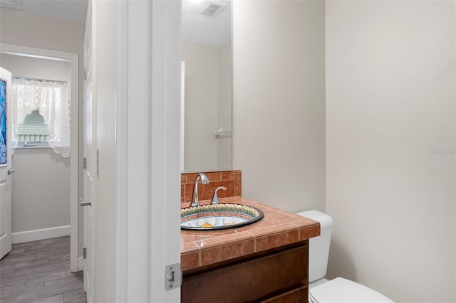 bathroom featuring visible vents, backsplash, toilet, vanity, and wood finished floors