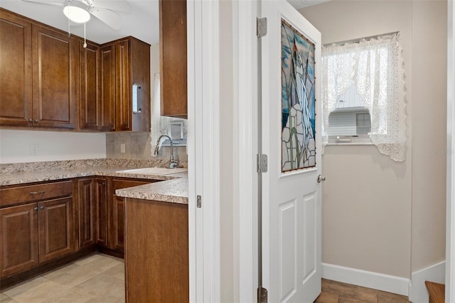 kitchen with light stone counters, a sink, a ceiling fan, and baseboards