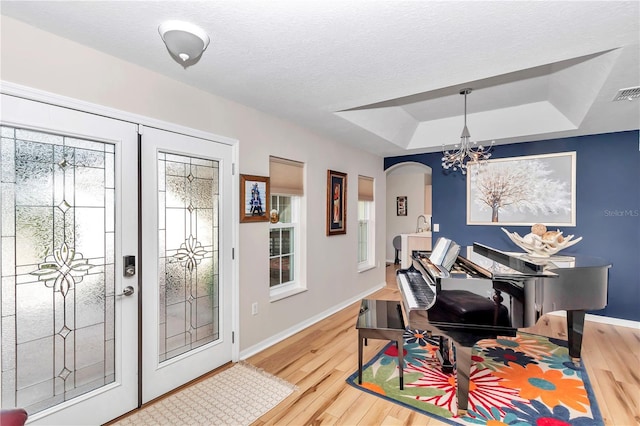 foyer featuring an inviting chandelier, a tray ceiling, wood-type flooring, and a textured ceiling