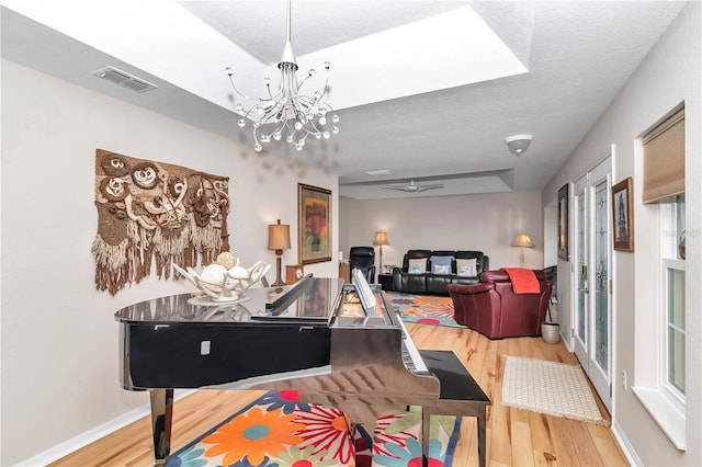 misc room featuring wood-type flooring, a raised ceiling, ceiling fan with notable chandelier, and a textured ceiling