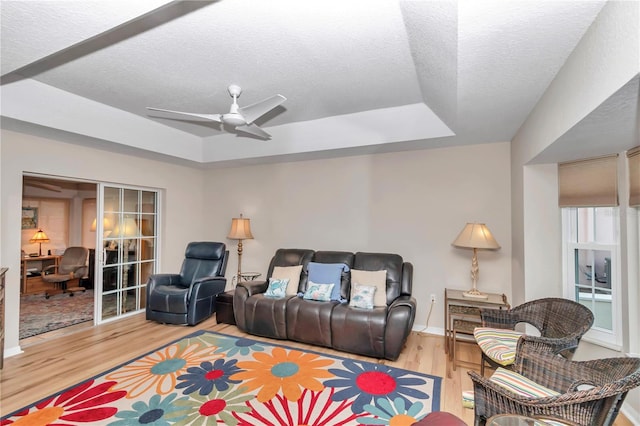 living room featuring ceiling fan, wood-type flooring, a raised ceiling, and a textured ceiling