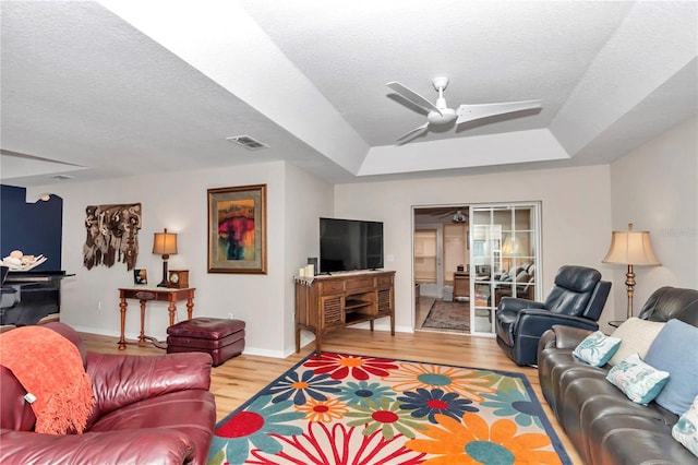 living room featuring ceiling fan, wood-type flooring, a raised ceiling, and a textured ceiling