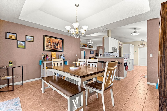 dining area with light tile patterned floors, a tray ceiling, and a chandelier