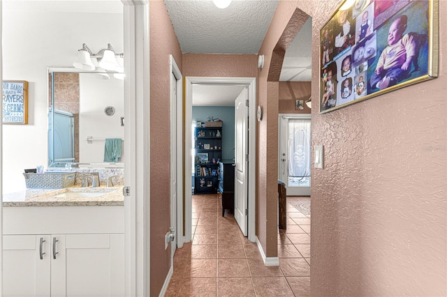 hallway with sink, a textured ceiling, and light tile patterned floors