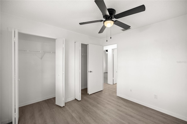 unfurnished bedroom with two closets, ceiling fan, and light wood-type flooring