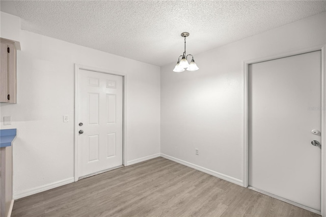 unfurnished dining area with an inviting chandelier, a textured ceiling, and light hardwood / wood-style flooring