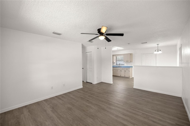 unfurnished living room featuring sink, ceiling fan with notable chandelier, dark hardwood / wood-style floors, and a textured ceiling