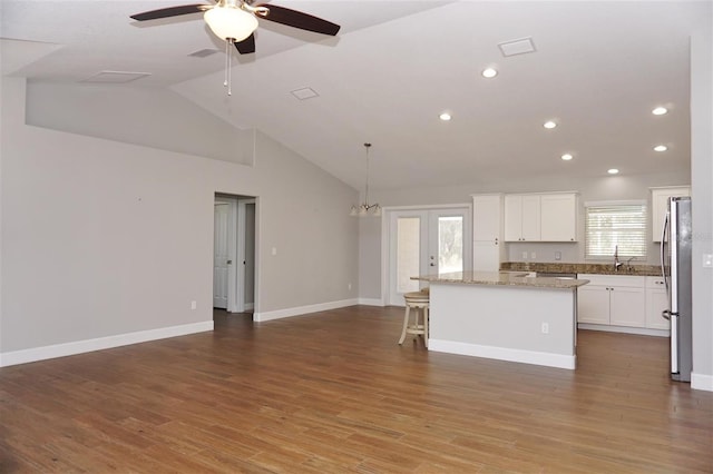 kitchen featuring pendant lighting, white cabinets, hardwood / wood-style flooring, a center island, and light stone counters