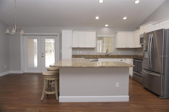 kitchen featuring vaulted ceiling, a kitchen island, white cabinetry, light stone counters, and stainless steel appliances