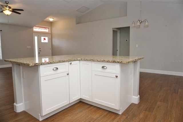 kitchen with pendant lighting, ceiling fan with notable chandelier, white cabinetry, light stone countertops, and dark wood-type flooring