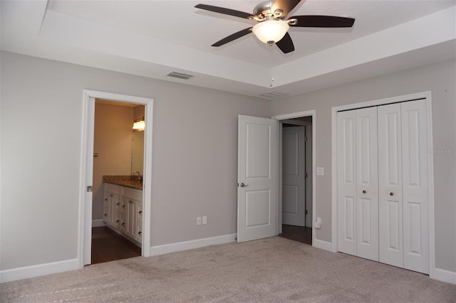 unfurnished bedroom with ensuite bathroom, light colored carpet, ceiling fan, a raised ceiling, and a closet