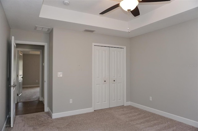 unfurnished bedroom with ceiling fan, a closet, a tray ceiling, and light carpet