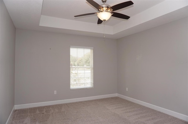 carpeted empty room with a raised ceiling and ceiling fan