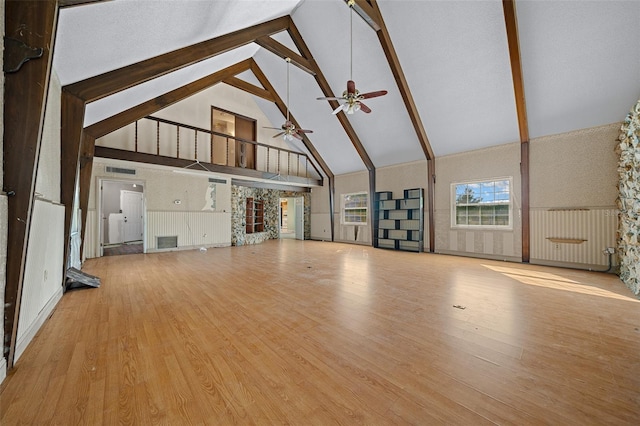 unfurnished living room featuring ceiling fan, high vaulted ceiling, beam ceiling, and light hardwood / wood-style floors