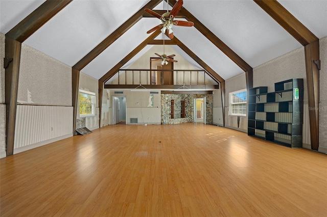 unfurnished living room with ceiling fan, wood-type flooring, high vaulted ceiling, and beamed ceiling