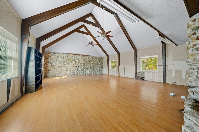 unfurnished living room featuring high vaulted ceiling, light hardwood / wood-style floors, beamed ceiling, and ceiling fan