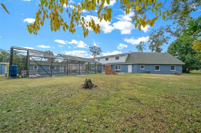 rear view of house featuring glass enclosure and a lawn