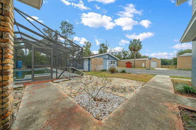 view of yard featuring an outbuilding, a garage, a patio area, and glass enclosure