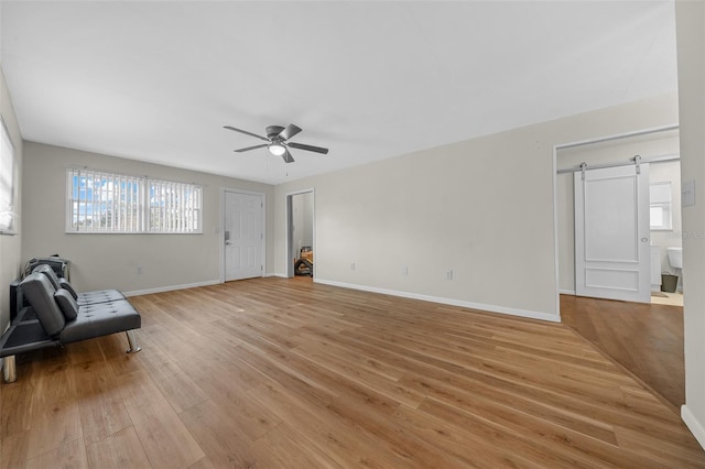 unfurnished room featuring ceiling fan, a barn door, and light wood-type flooring