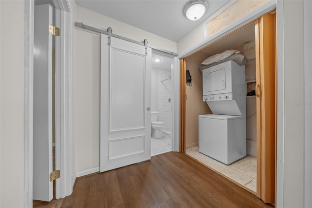 clothes washing area featuring hardwood / wood-style flooring, stacked washing maching and dryer, and a barn door