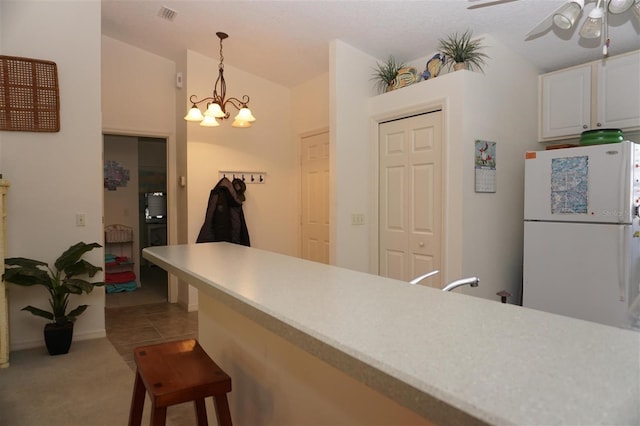 kitchen with a kitchen bar, lofted ceiling, white cabinetry, white fridge, and pendant lighting