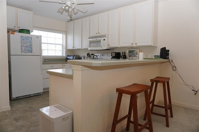 kitchen with white appliances, a kitchen bar, kitchen peninsula, and white cabinets