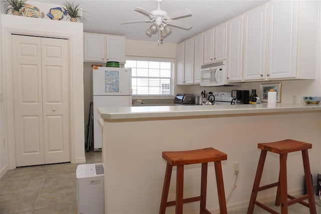 kitchen with light tile patterned floors, white appliances, a kitchen breakfast bar, white cabinets, and kitchen peninsula