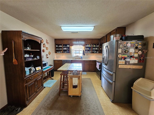 kitchen with a kitchen island, appliances with stainless steel finishes, dark brown cabinetry, and a textured ceiling