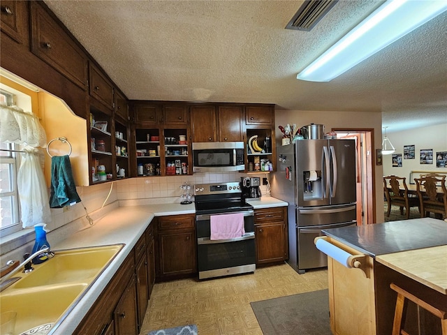 kitchen featuring sink, a textured ceiling, dark brown cabinets, appliances with stainless steel finishes, and backsplash