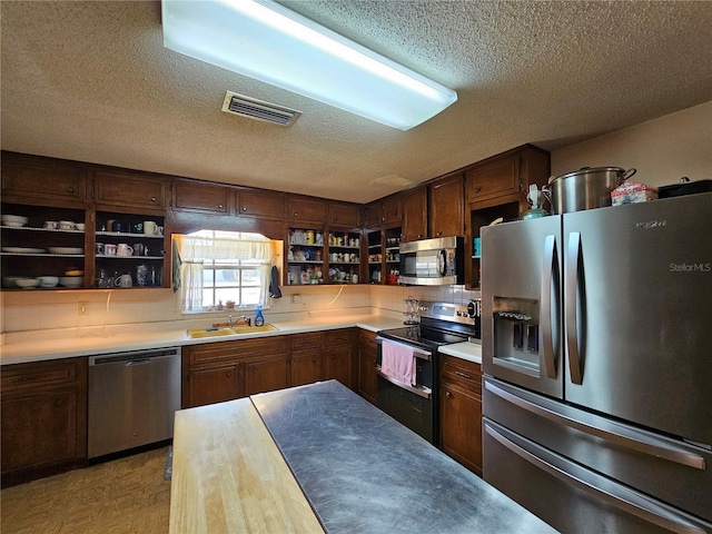 kitchen with dark brown cabinetry, stainless steel appliances, sink, and a textured ceiling