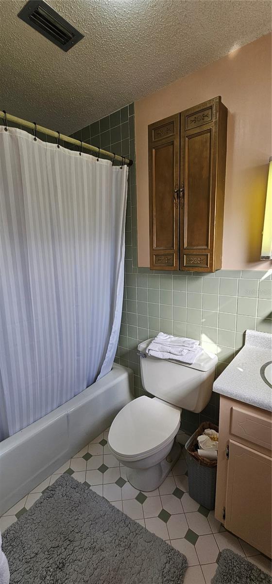 full bathroom with vanity, tile walls, a textured ceiling, and toilet