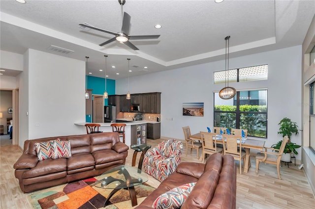 living room featuring a raised ceiling, ceiling fan, a textured ceiling, and light wood-type flooring