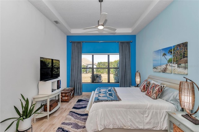 bedroom featuring ceiling fan, light hardwood / wood-style floors, a raised ceiling, and a textured ceiling