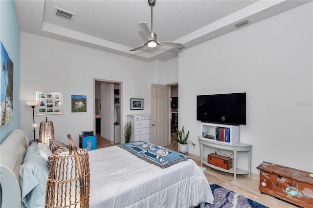 bedroom with a tray ceiling, ceiling fan, light hardwood / wood-style floors, a textured ceiling, and a closet