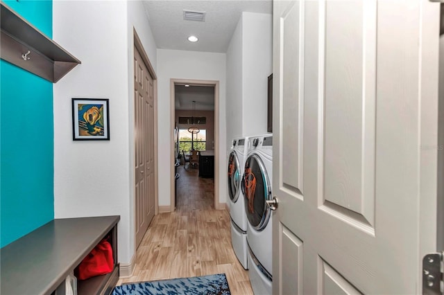 laundry room featuring washing machine and clothes dryer, light hardwood / wood-style flooring, and a textured ceiling