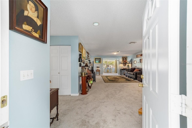 hall with light colored carpet and a textured ceiling