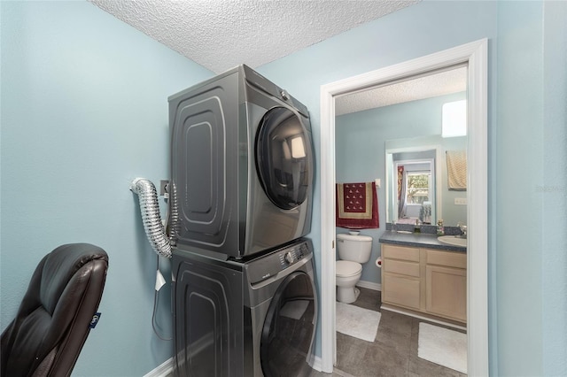 laundry area featuring sink, a textured ceiling, and stacked washing maching and dryer