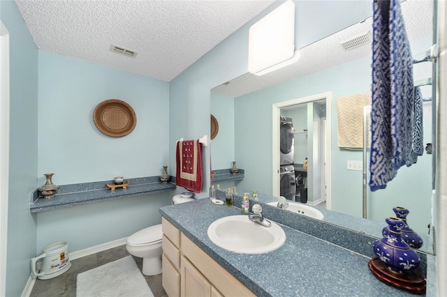 bathroom featuring stacked washer / dryer, vanity, toilet, tile patterned floors, and a textured ceiling