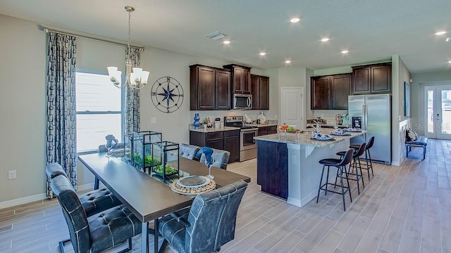 kitchen with hanging light fixtures, a center island with sink, stainless steel appliances, light hardwood / wood-style floors, and a kitchen bar