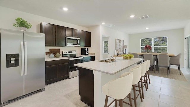 kitchen with sink, a kitchen bar, stainless steel appliances, an island with sink, and light tile patterned flooring