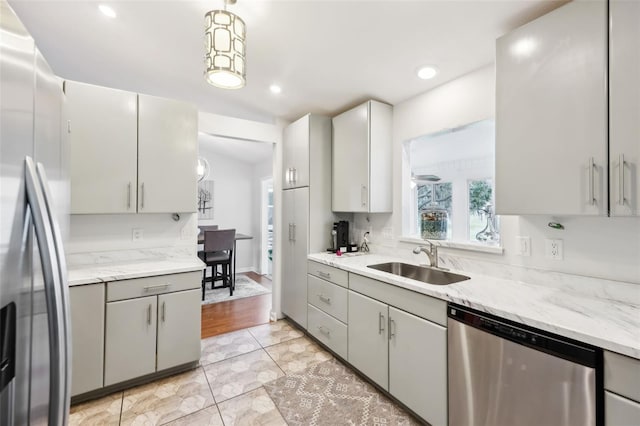 kitchen with light stone countertops, appliances with stainless steel finishes, sink, and decorative light fixtures