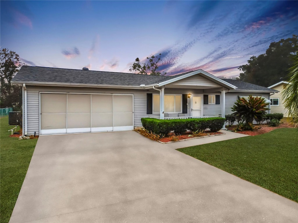 ranch-style house featuring cooling unit, a garage, covered porch, and a lawn