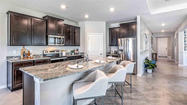 kitchen with an island with sink, sink, a kitchen breakfast bar, dark brown cabinetry, and stainless steel appliances