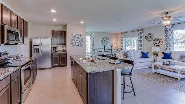 kitchen with sink, light tile patterned floors, stainless steel appliances, an island with sink, and a kitchen bar