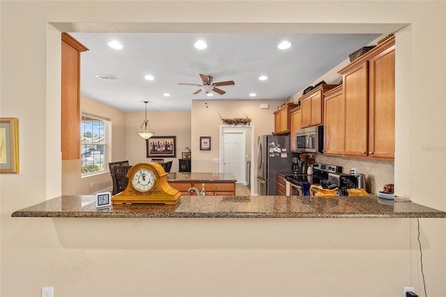 kitchen featuring backsplash, dark stone counters, hanging light fixtures, kitchen peninsula, and stainless steel appliances